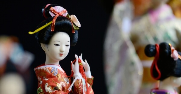 A Japanese doll wearing a kimono and holding red thread in her hands.