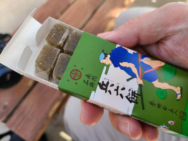 Box of hyōroku mochi, with a picture of a samurai on it. Inside are dark green candies wrapped in clearish rice paper