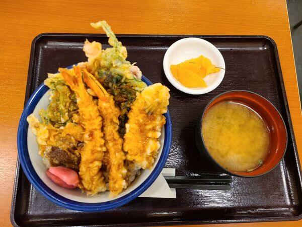 Bowl of ten-don, assorted tempura on rice. Beside it is a bowl of miso soup and a small plate of yellow pickled vegetables