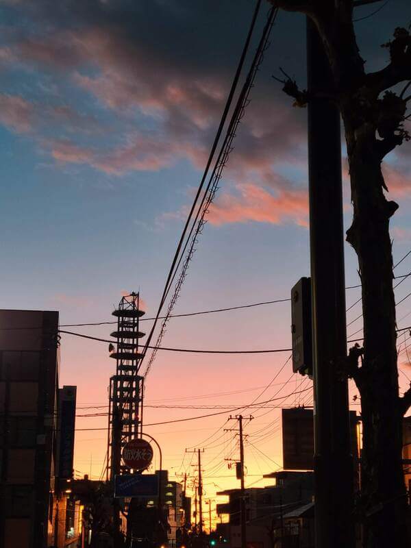 The sky is orange and purple from the sunset, and the buildings, street signs, and power lines are silhouetted black against the colorful sky