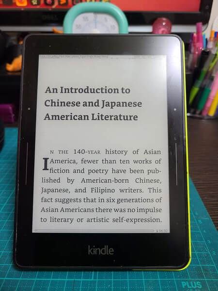 An Amazon Kindle Voyage standing upright and displaying the text of "An Anthology of Aiiieeeee!" showing the crisp, clear text of the e-ink