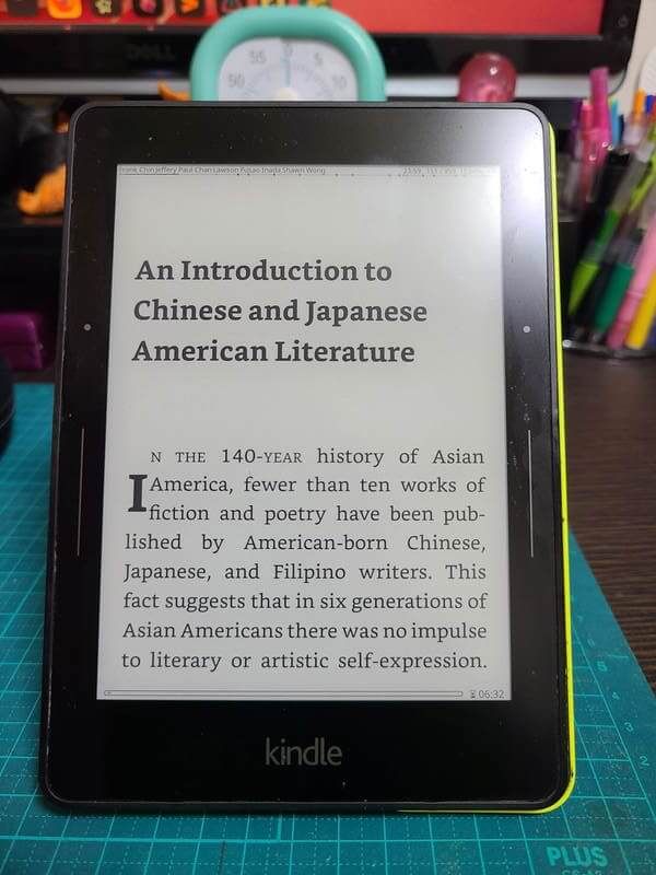 An Amazon Kindle Voyage standing upright and displaying the text of "An Anthology of Aiiieeeee!" showing the crisp, clear text of the eInk