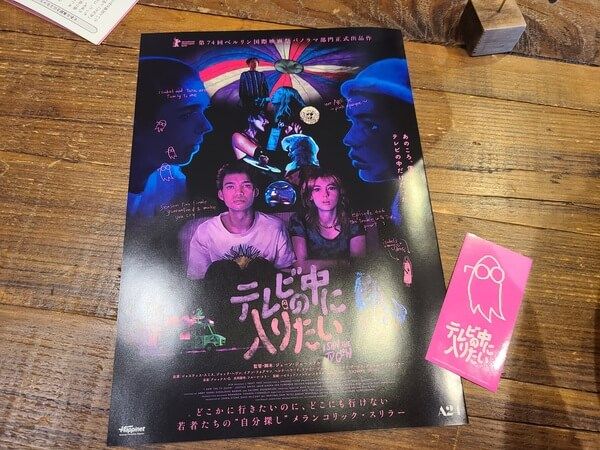 Pamphlet and ticket/sticker for I Saw the TV Glow (Terebi no Naka ni Hairitai) in Japanese. The ticket/sticker is a bright pink rectangle with the movie's ghost in white outline
