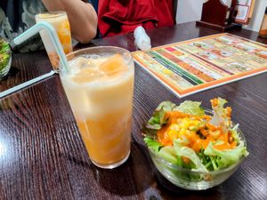 Glass of mango lassi next to a small bowl of salad with orange dressing