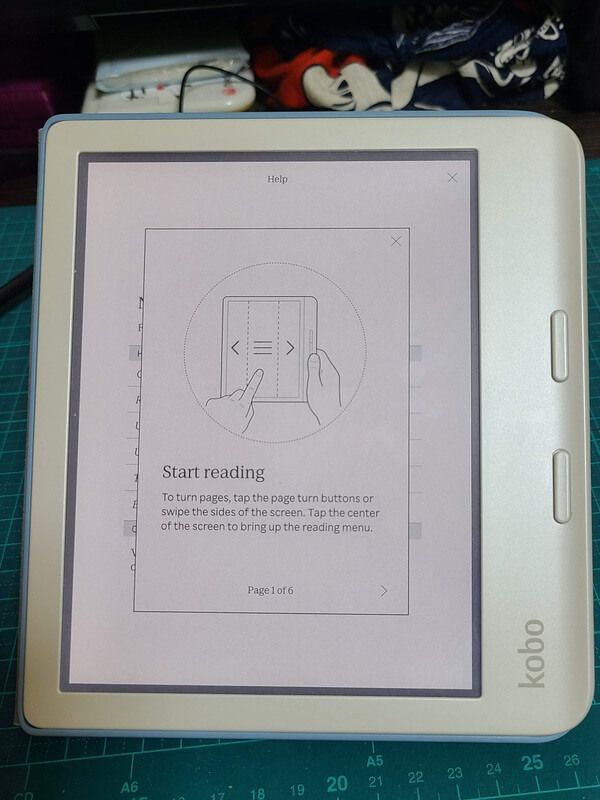 A white Kobo Libra Colour with the "Reading a book" tutorial open on the screen showing how to swipe to turn the page