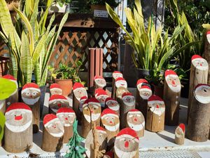 A cluster of small logs with Santa faces painted on the ends, surrounded by potted plants