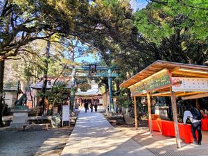 The main green-bronze torii gate leading to the head shrine. On the right are some wooden stands with pamphlets and covered in red cloth, and all around the sides are trees and plants