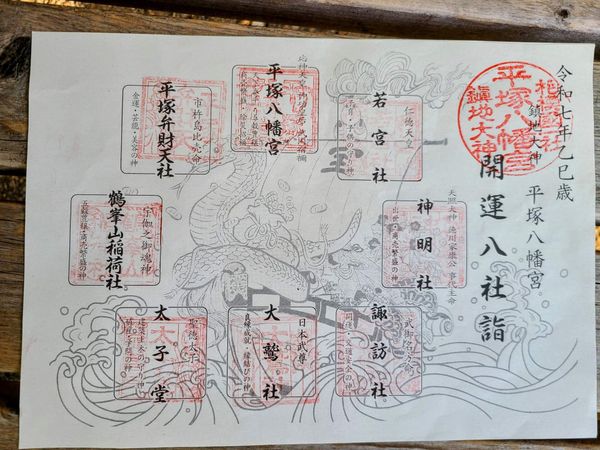 A sheet of paper with a takarabune (the treasure boat that the Seven Lucky Gods ride through the sky) with a large snake head at the front. Around the page are eight spots for with faded red stamps, each marked with the name of the matching god